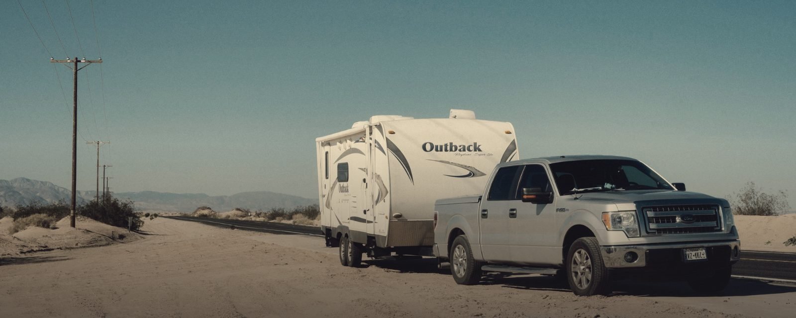 A pickup truck towing a trailer on a desert highway
