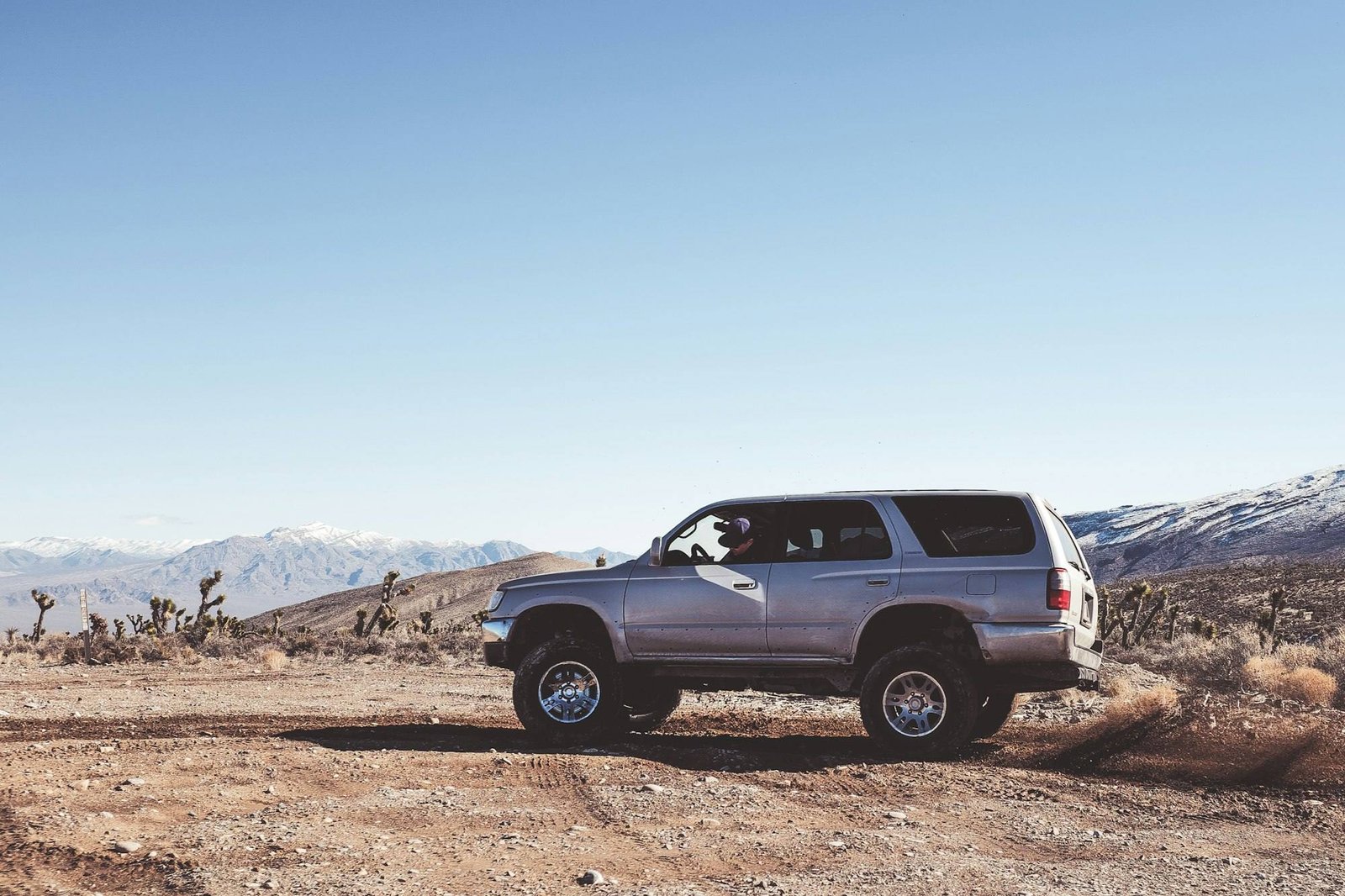 An earlier-generation lifted gray Toyota 4Runner on a desert dirt track with snow-capped mountains behind