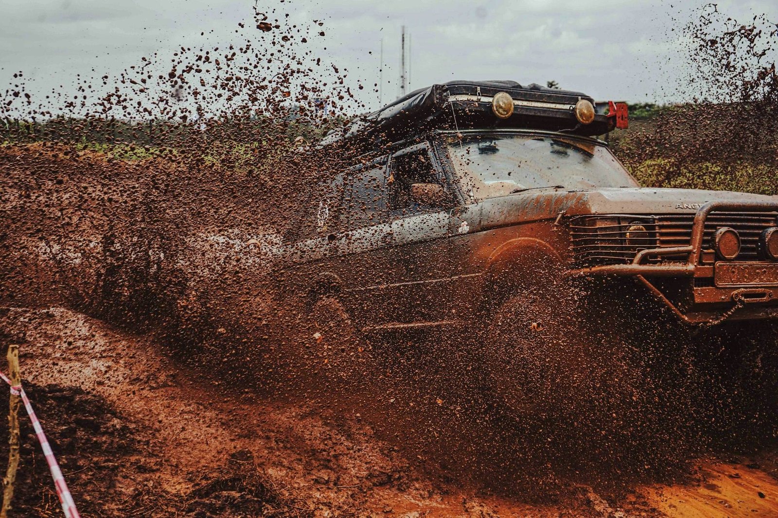 An old 4x4 with a roof rack ploughing through thick red mud and throwing it into the air