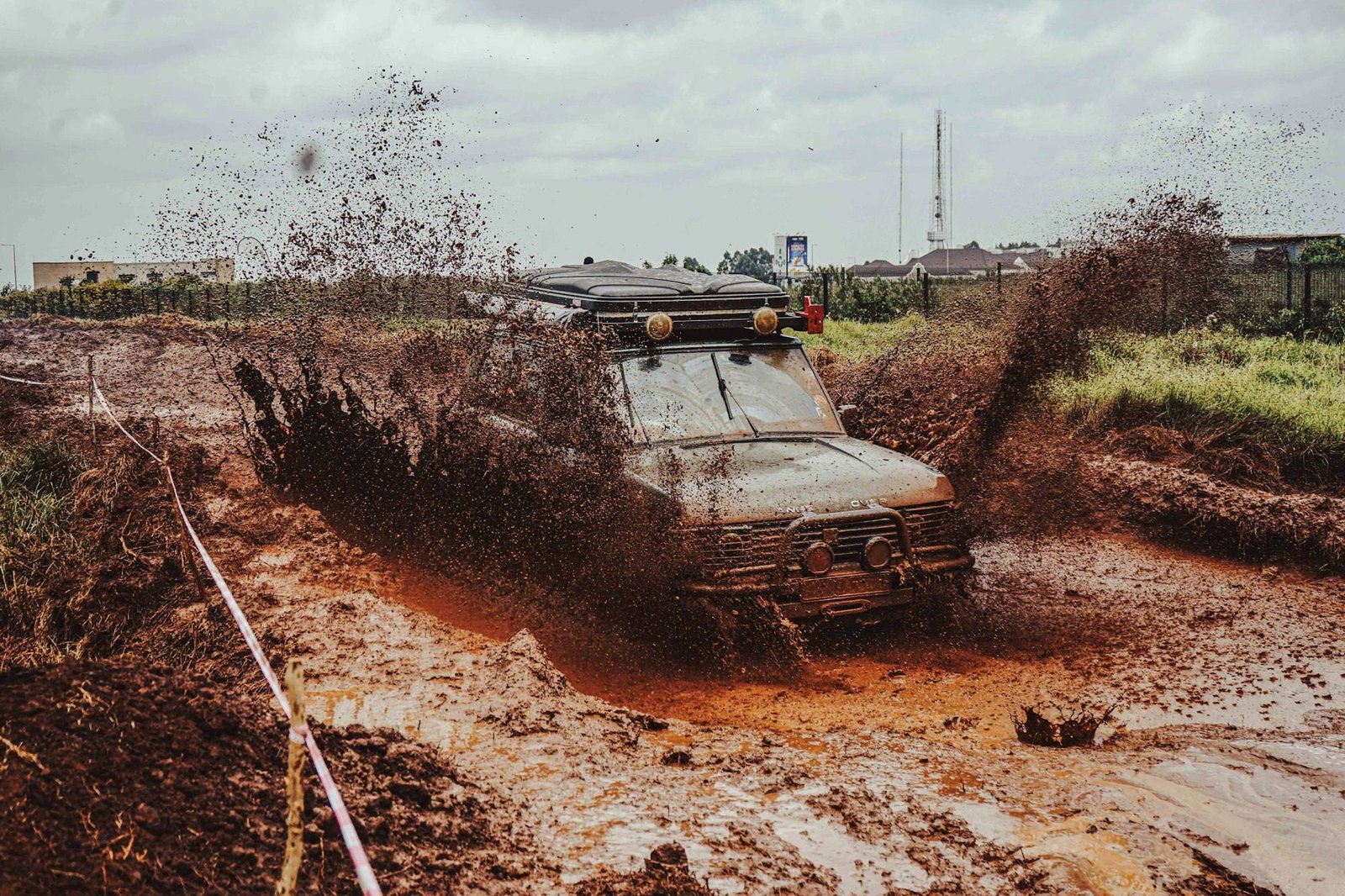 An old 4x4 with a roof rack driving head-on through a deep muddy track