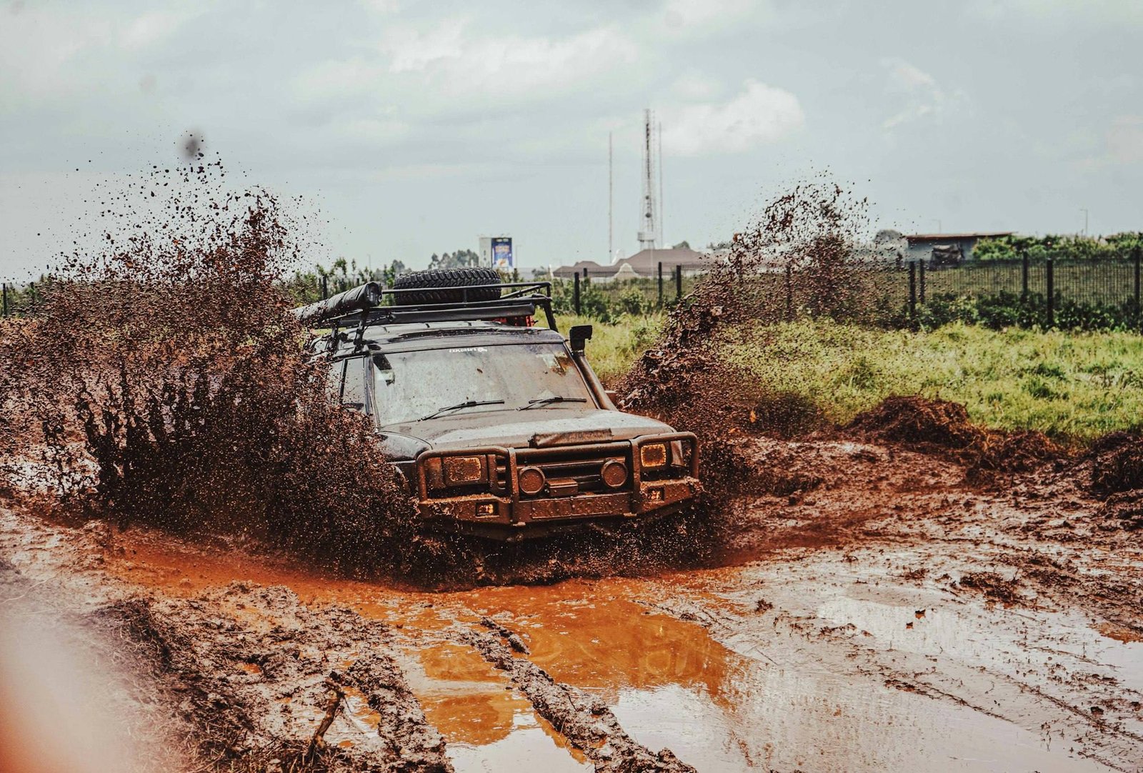 An old 4x4 with a roof rack splashing through muddy terrain