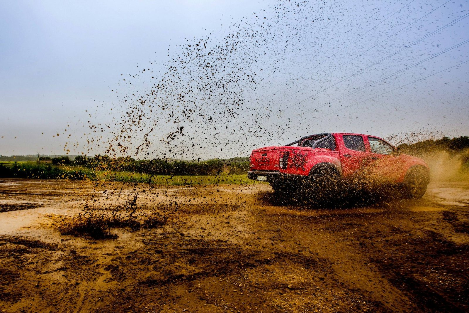 A red four-door pickup throwing mud across a dirt track