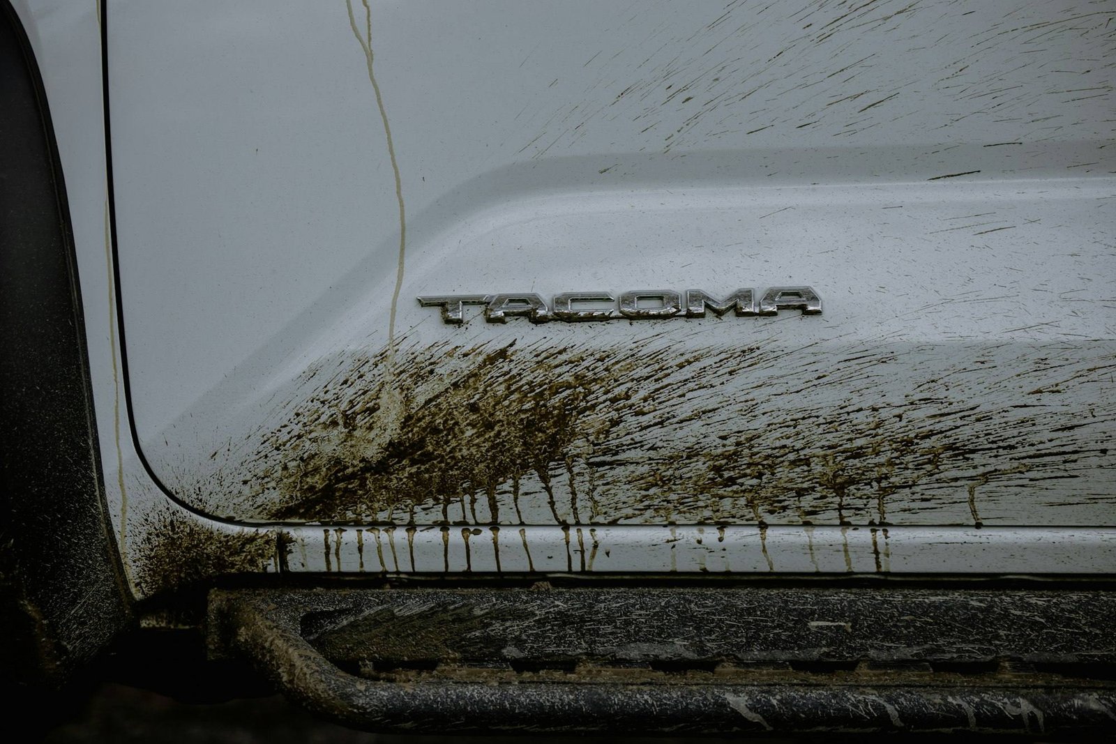 The Tacoma badge on a white Toyota pickup, splattered with mud