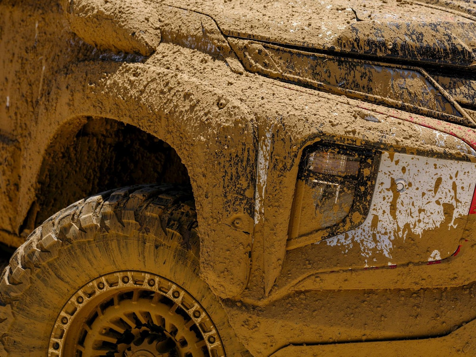 A mud-covered pickup with a large off-road tire and bronze wheel